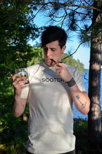 Man drinking a glass of scotch in a shirt that says "scotch".