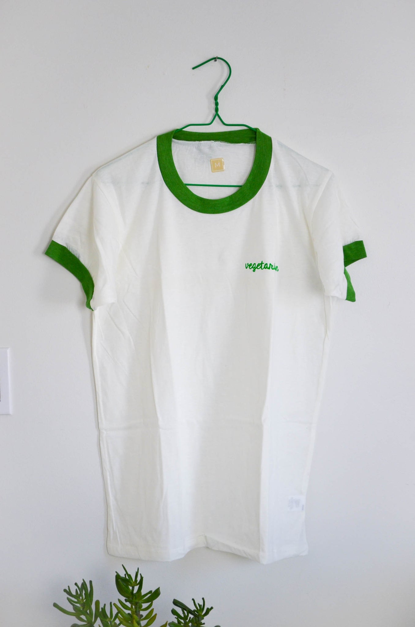 White t-shirt with green trim on a hanger against a white background