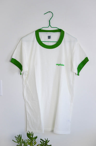 White t-shirt with green trim on a hanger against a white wall.